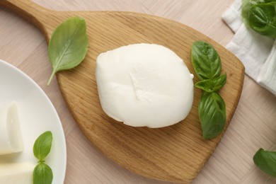 Photo of Piece of delicious mozzarella cheese and basil on wooden table, flat lay