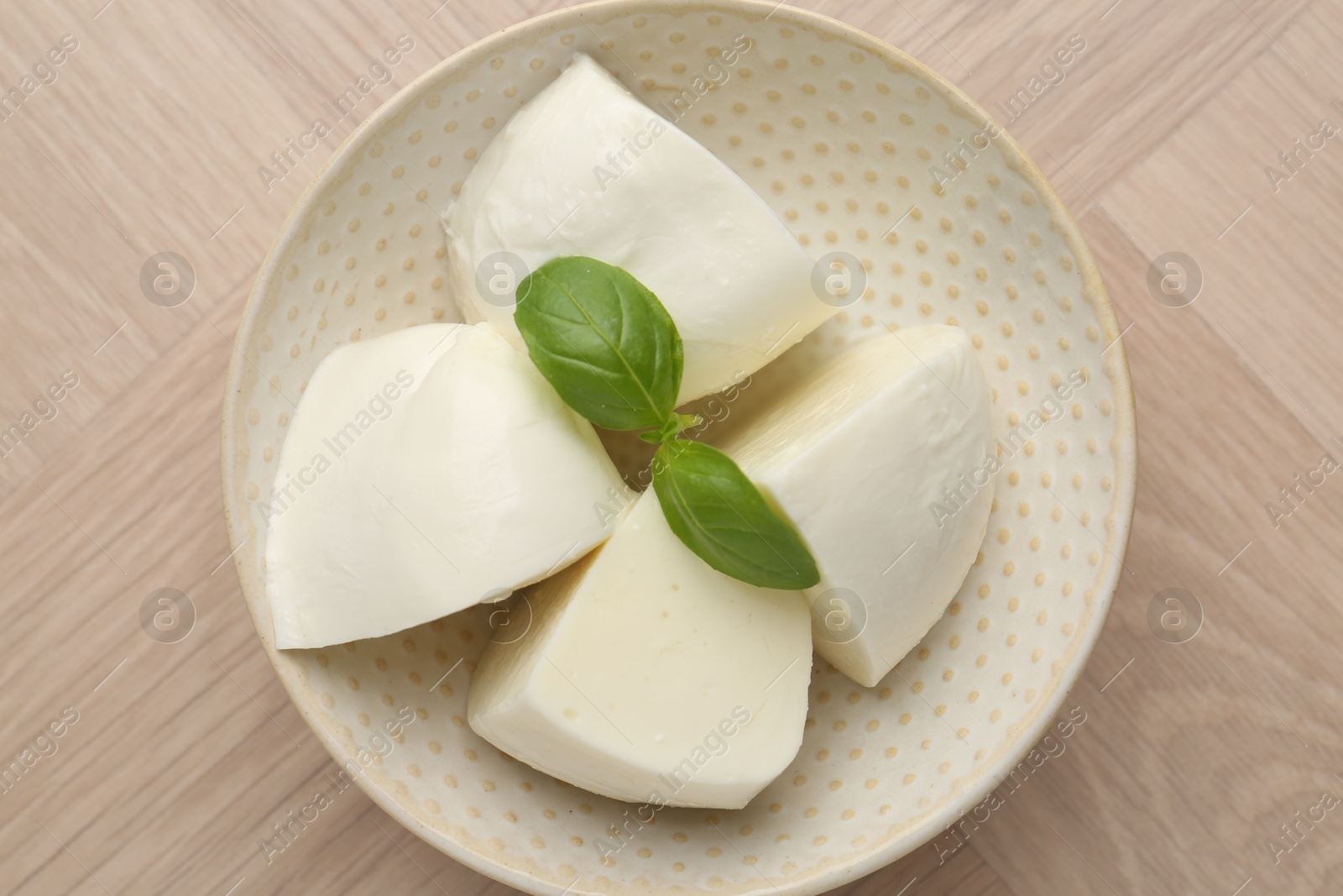 Pieces of delicious mozzarella cheese and basil in bowl on wooden table, top view Photo of Pieces of delicious mozzarella cheese and basil in bowl on wooden table, top view
