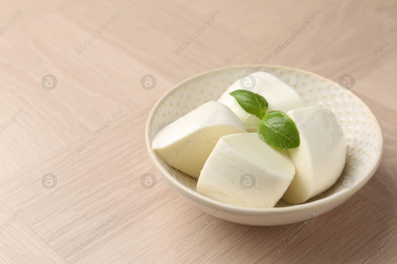 Pieces of delicious mozzarella cheese and basil in bowl on wooden table, closeup. Space for text Photo of Pieces of delicious mozzarella cheese and basil in bowl on wooden table, closeup. Space for text