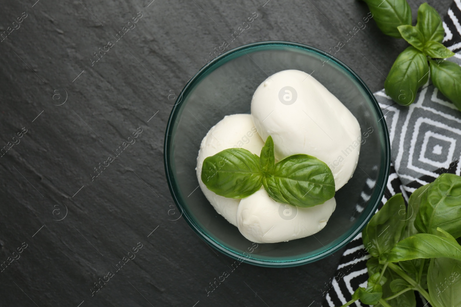 Pieces of delicious mozzarella cheese and basil in bowl on dark textured table, flat lay. Space for text Photo of Pieces of delicious mozzarella cheese and basil in bowl on dark textured table, flat lay. Space for text