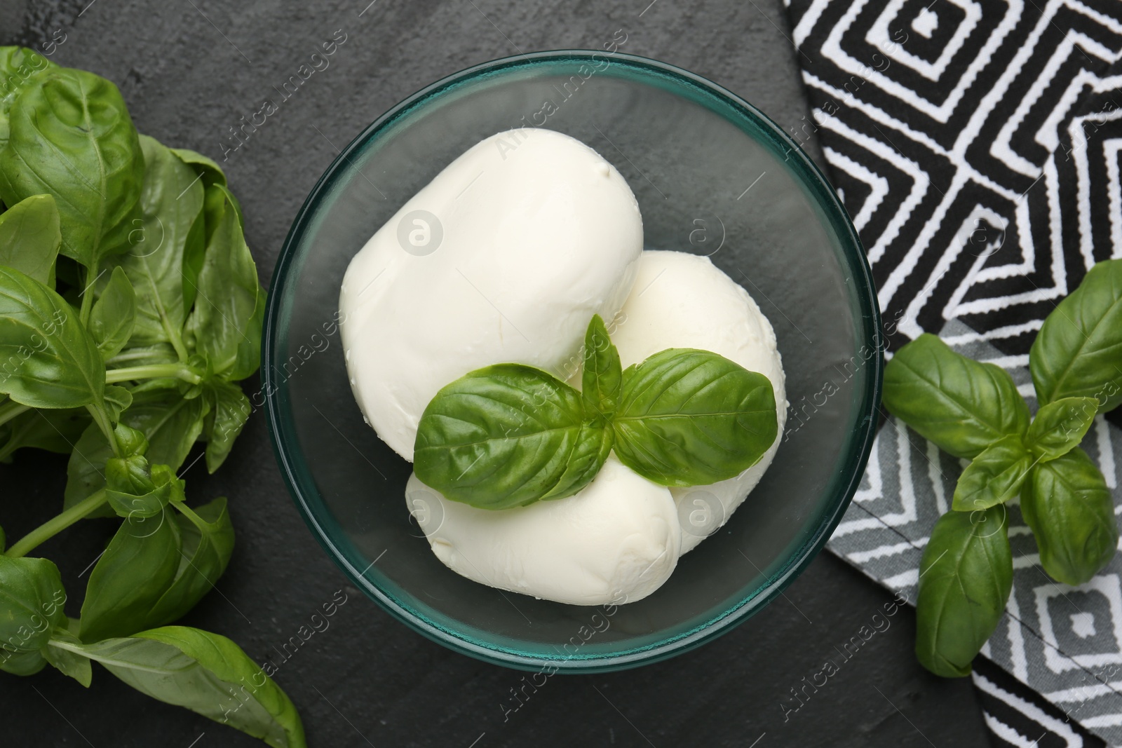 Pieces of delicious mozzarella cheese and basil in bowl on dark textured table, flat lay Photo of Pieces of delicious mozzarella cheese and basil in bowl on dark textured table, flat lay