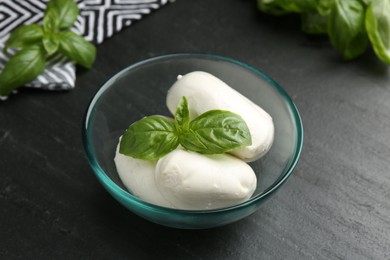 Photo of Pieces of delicious mozzarella cheese and basil in bowl on dark textured table, closeup