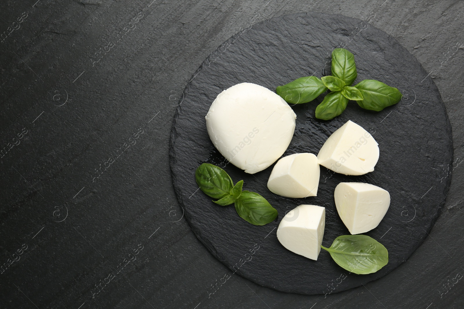 Pieces of delicious mozzarella cheese and basil on dark textured table, top view. Space for text Photo of Pieces of delicious mozzarella cheese and basil on dark textured table, top view. Space for text