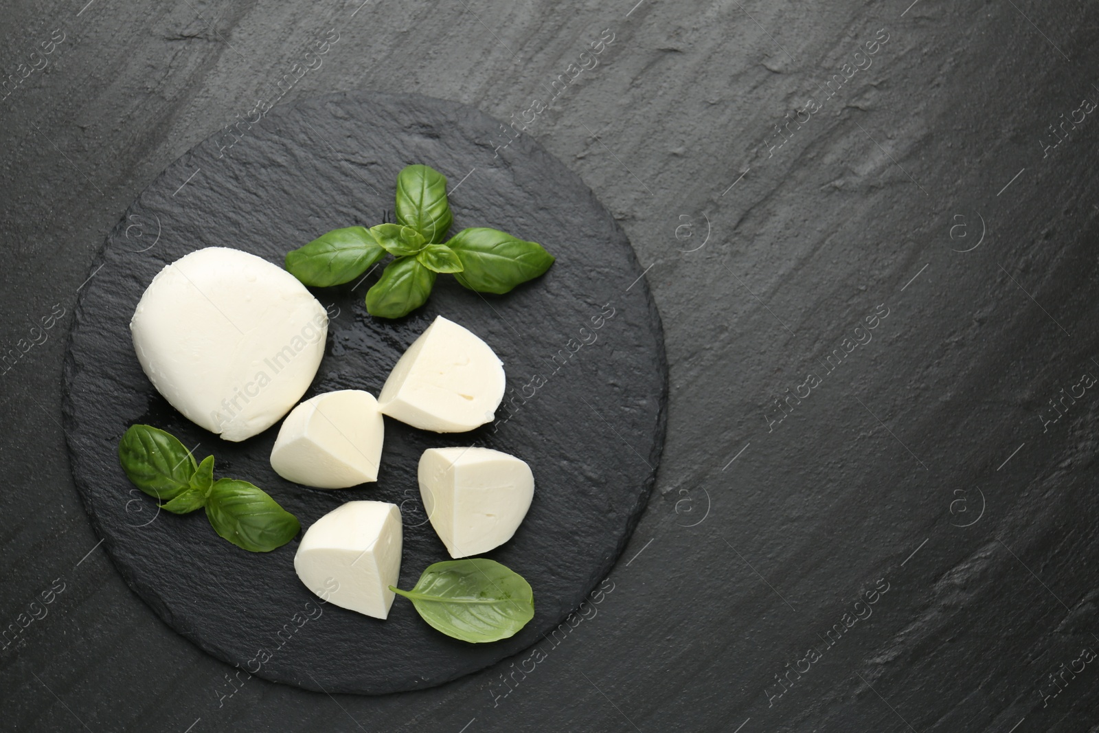 Pieces of delicious mozzarella cheese and basil on dark textured table, top view. Space for text Photo of Pieces of delicious mozzarella cheese and basil on dark textured table, top view. Space for text