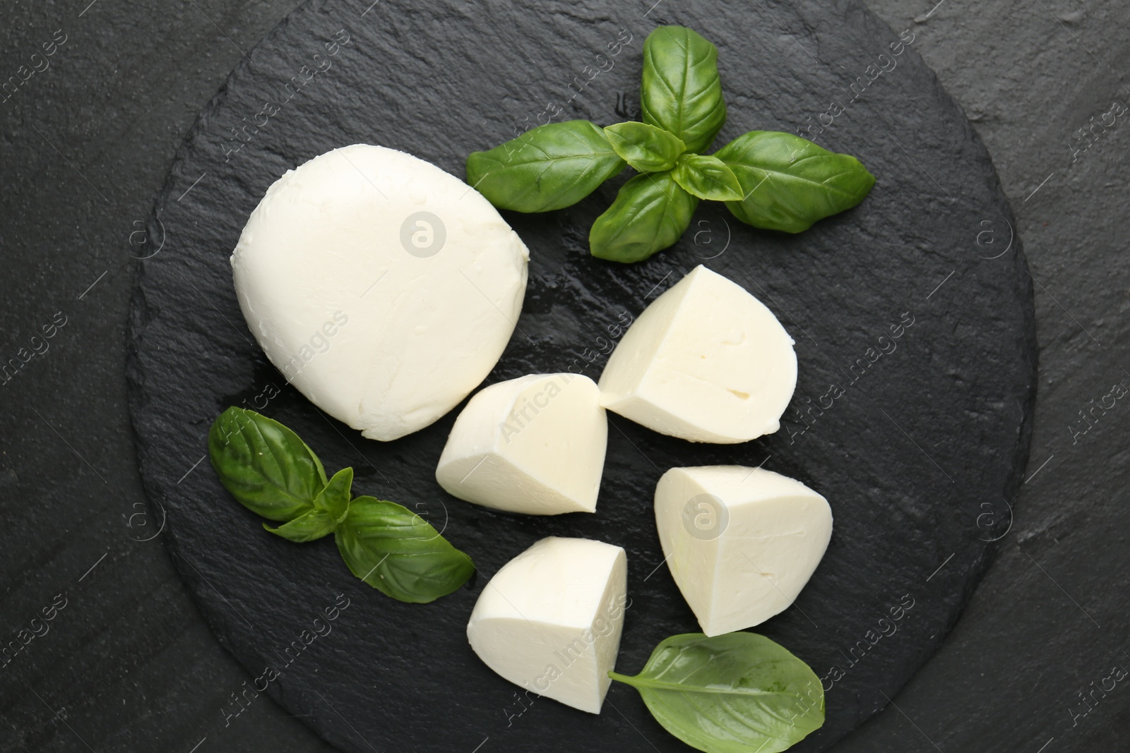 Pieces of delicious mozzarella cheese and basil on dark textured table, top view Photo of Pieces of delicious mozzarella cheese and basil on dark textured table, top view