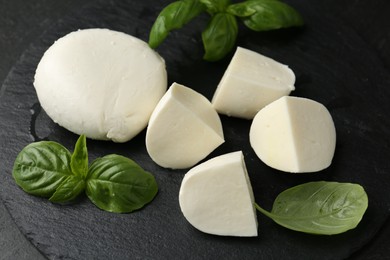 Photo of Pieces of delicious mozzarella cheese and basil on dark table, closeup