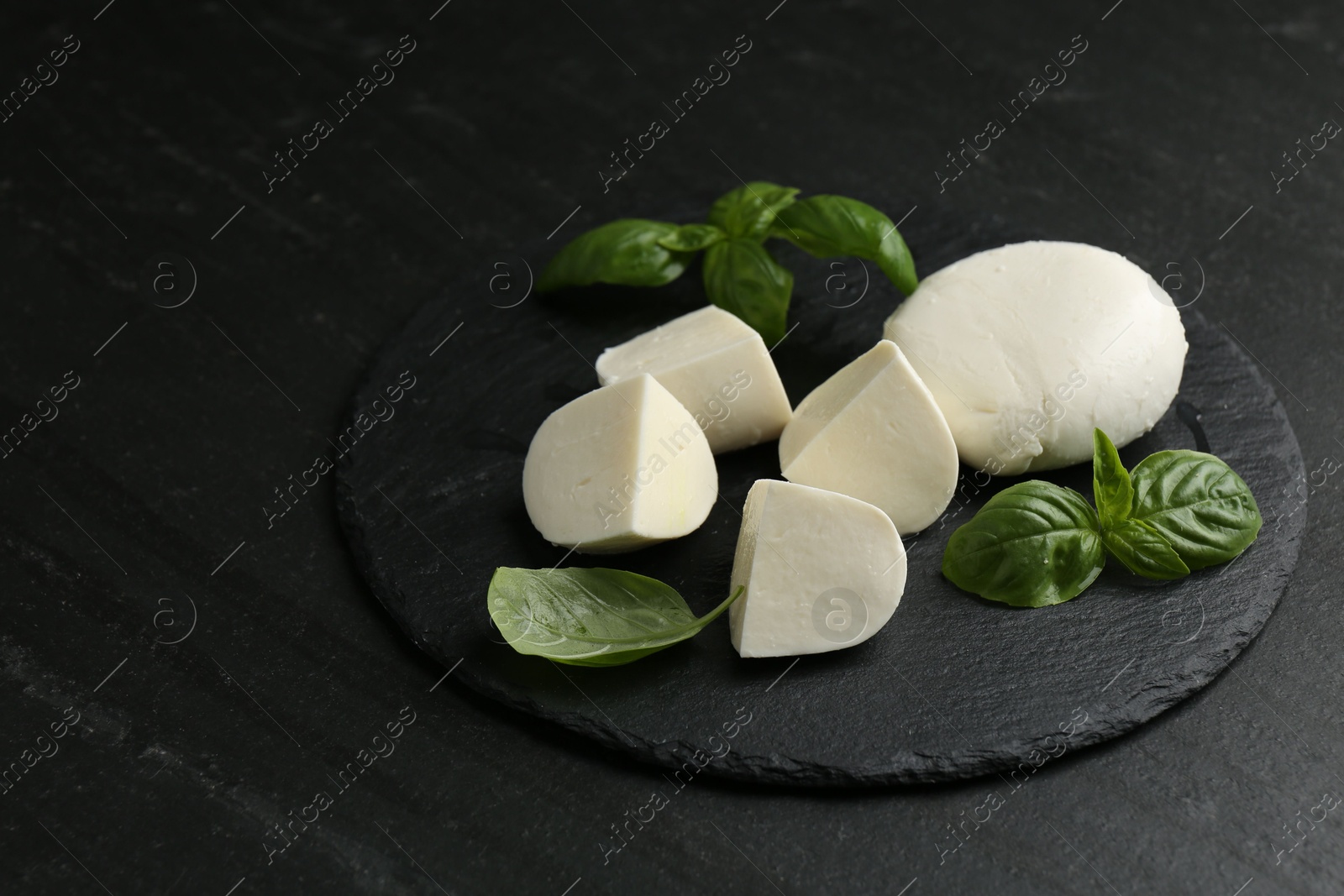 Pieces of delicious mozzarella cheese and basil on dark textured table, closeup Photo of Pieces of delicious mozzarella cheese and basil on dark textured table, closeup
