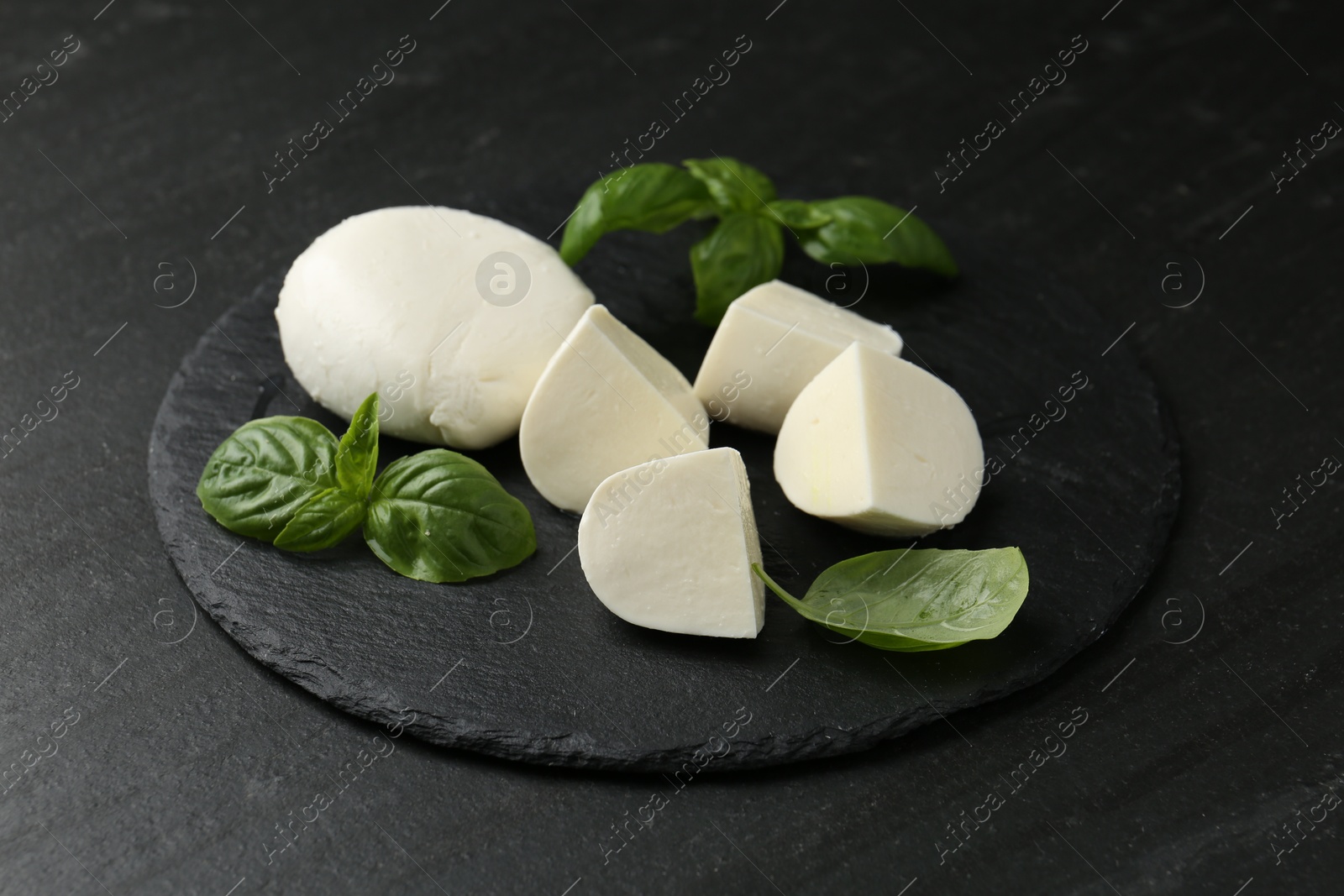 Pieces of delicious mozzarella cheese and basil on dark textured table, closeup Photo of Pieces of delicious mozzarella cheese and basil on dark textured table, closeup