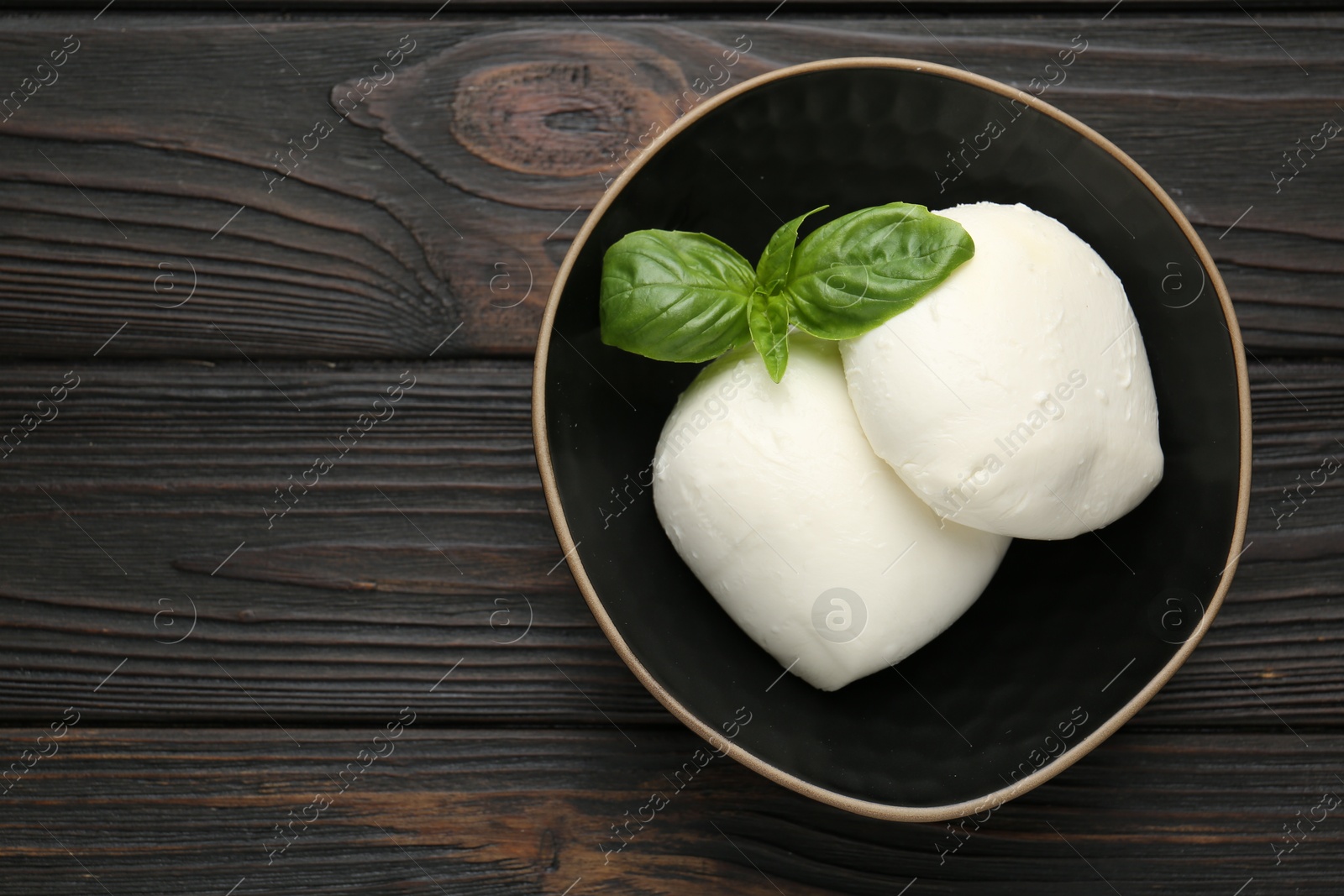 Pieces of delicious mozzarella cheese and basil in bowl on wooden table, top view. Space for text Photo of Pieces of delicious mozzarella cheese and basil in bowl on wooden table, top view. Space for text
