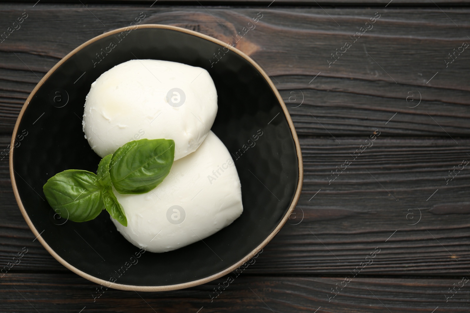 Pieces of delicious mozzarella cheese and basil in bowl on wooden table, top view. Space for text Photo of Pieces of delicious mozzarella cheese and basil in bowl on wooden table, top view. Space for text