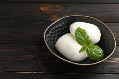 Photo of Pieces of delicious mozzarella cheese and basil in bowl on wooden table, closeup. Space for text