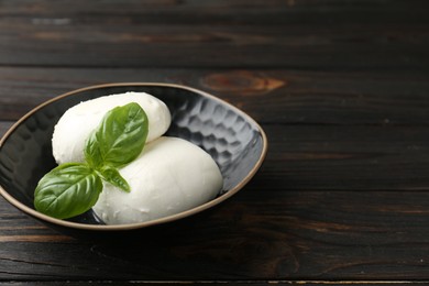 Photo of Pieces of delicious mozzarella cheese and basil in bowl on wooden table, closeup. Space for text