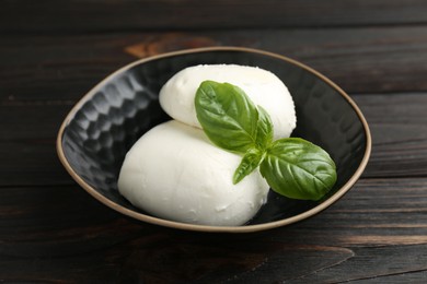 Photo of Pieces of delicious mozzarella cheese and basil in bowl on wooden table, closeup