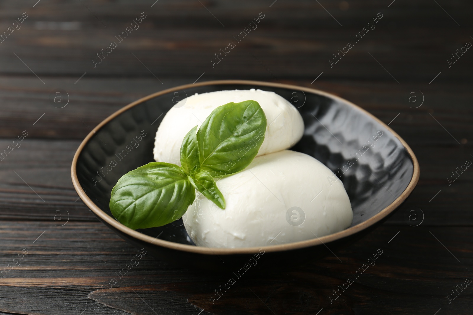 Pieces of delicious mozzarella cheese and basil in bowl on wooden table, closeup Photo of Pieces of delicious mozzarella cheese and basil in bowl on wooden table, closeup
