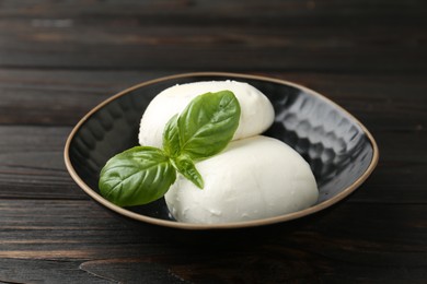 Photo of Pieces of delicious mozzarella cheese and basil in bowl on wooden table, closeup