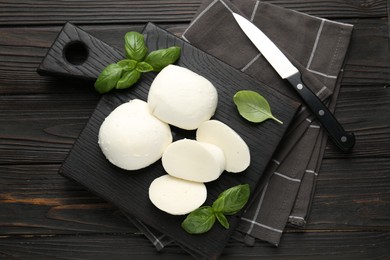 Photo of Pieces of delicious mozzarella cheese and basil on wooden table, flat lay