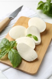 Photo of Pieces of delicious mozzarella cheese, basil leaves and knife on white wooden table, closeup