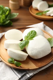 Photo of Pieces of delicious mozzarella cheese and basil leaves on wooden table, closeup