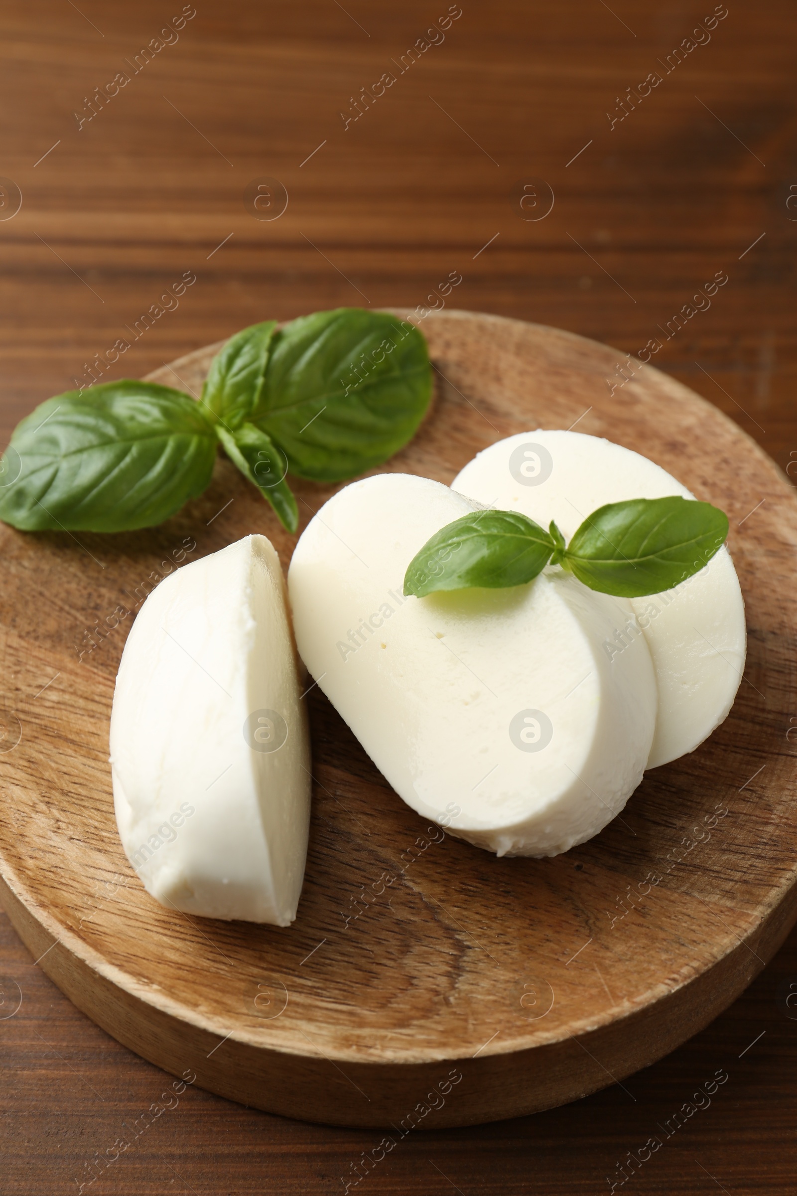 Pieces of delicious mozzarella cheese and basil leaves on wooden table, closeup Photo of Pieces of delicious mozzarella cheese and basil leaves on wooden table, closeup