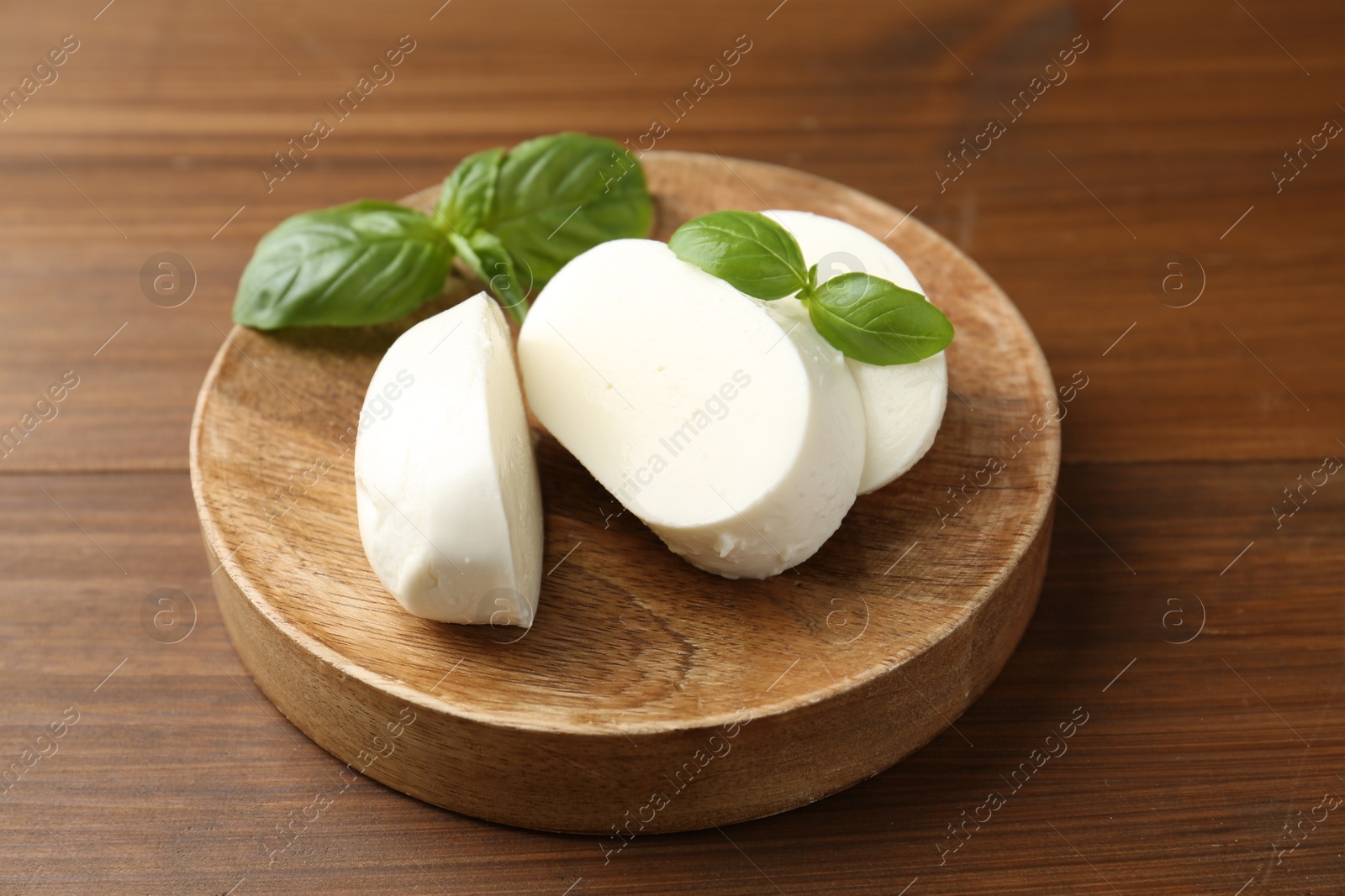 Pieces of delicious mozzarella cheese and basil leaves on wooden table, closeup Photo of Pieces of delicious mozzarella cheese and basil leaves on wooden table, closeup