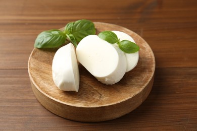 Photo of Pieces of delicious mozzarella cheese and basil leaves on wooden table, closeup