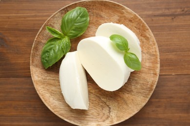 Photo of Pieces of delicious mozzarella cheese and basil leaves on wooden table, top view