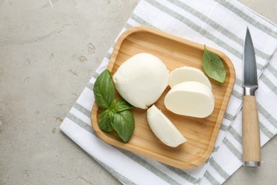 Photo of Pieces of delicious mozzarella cheese, basil leaves and knife on grey textured table, top view
