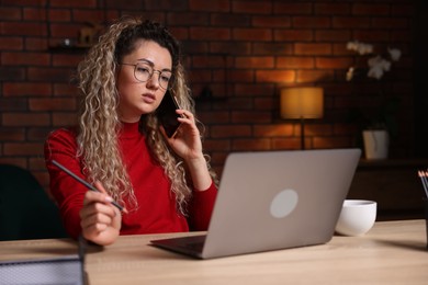 Photo of Woman talking by smartphone at desk with laptop in home office