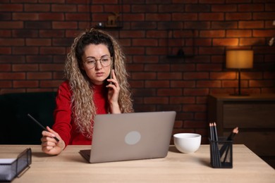 Photo of Woman talking by smartphone at desk with laptop in home office
