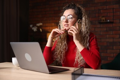 Photo of Woman talking by smartphone at desk with laptop in home office