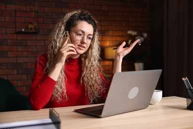 Photo of Woman talking by smartphone at desk with laptop in home office