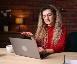 Photo of Smiling woman having videochat by laptop at desk in home office