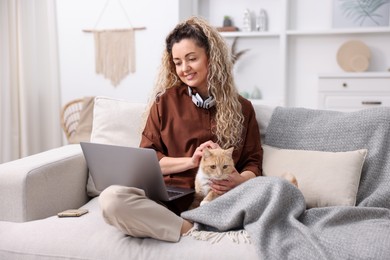 Photo of Smiling woman working with laptop and cat on sofa in home office