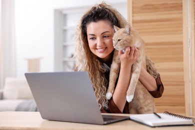 Photo of Smiling woman showing her cat by videochat at desk in home office