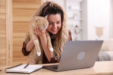 Photo of Smiling woman showing her cat by videochat at desk in home office