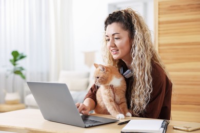 Photo of Woman having videochat by laptop and cat at desk in home office