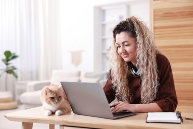 Photo of Smiling woman working with laptop and cat at desk in home office