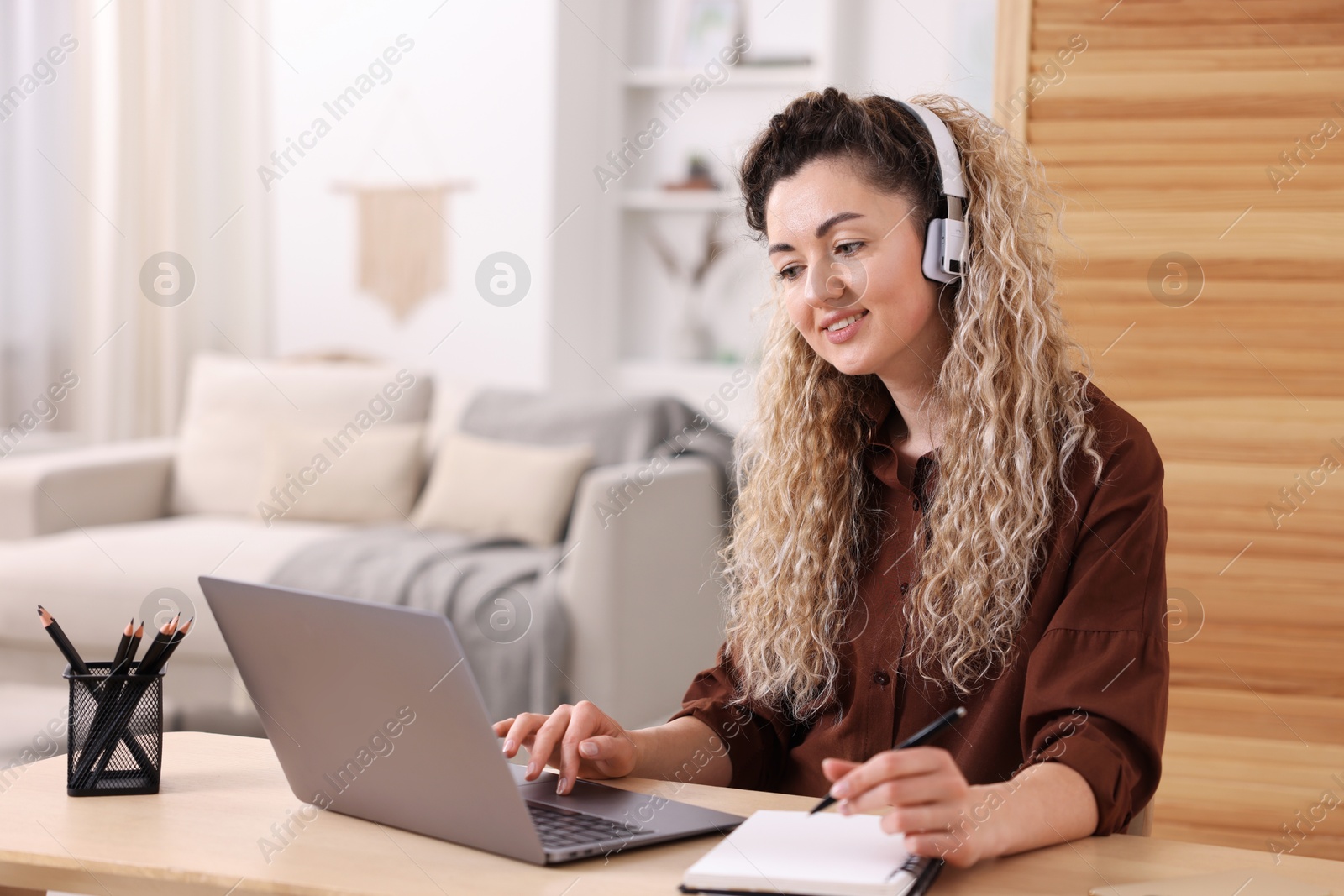 Smiling woman in headphones having videochat by laptop at desk in home office Photo of Smiling woman in headphones having videochat by laptop at desk in home office