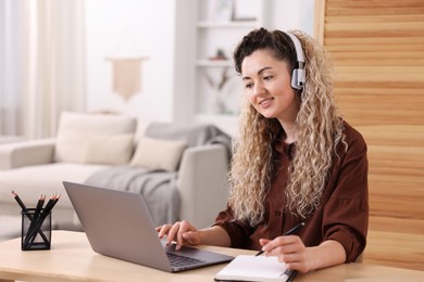 Photo of Smiling woman in headphones having videochat by laptop at desk in home office
