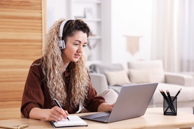 Photo of Woman in headphones working with laptop at desk in home office