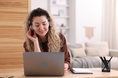 Photo of Smiling woman in headphones working with laptop at desk in home office