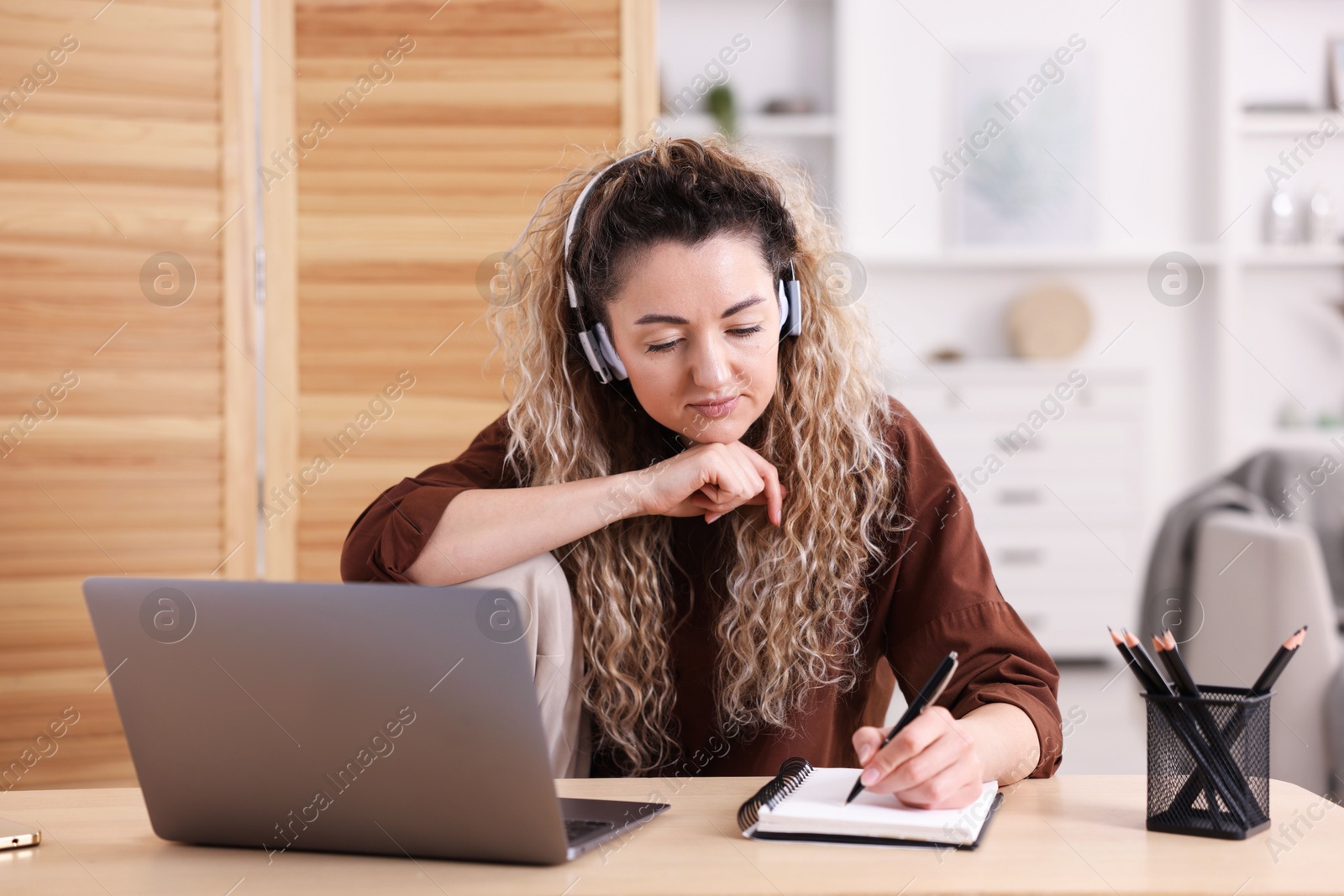 Woman in headphones working with laptop at desk in home office Photo of Woman in headphones working with laptop at desk in home office