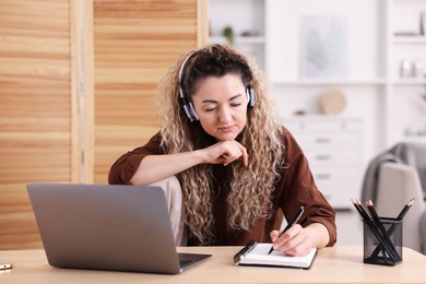 Photo of Woman in headphones working with laptop at desk in home office