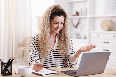 Photo of Smiling woman having videochat by laptop at desk in home office