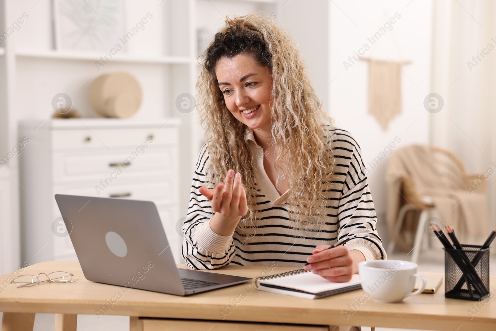 Smiling woman having videochat by laptop at desk in home office Photo of Smiling woman having videochat by laptop at desk in home office