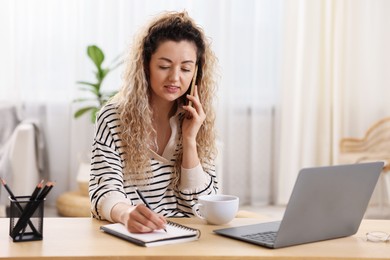 Photo of Smiling woman talking by smartphone and working at desk in home office
