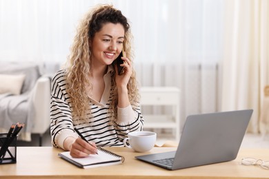 Photo of Smiling woman talking by smartphone and working at desk in home office