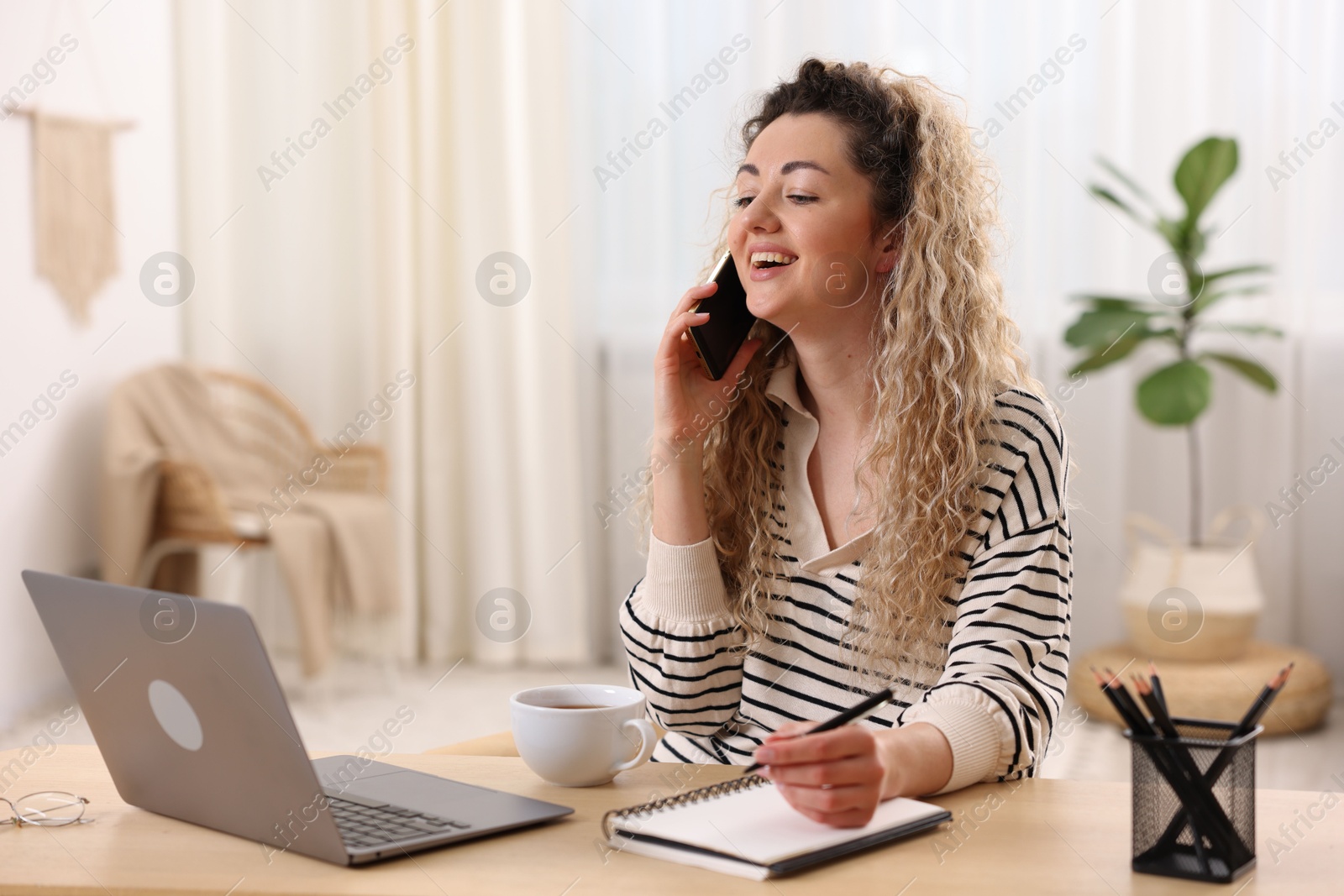Smiling woman talking by smartphone and working at desk in home office Photo of Smiling woman talking by smartphone and working at desk in home office