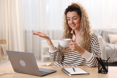 Photo of Smiling woman having videochat by laptop at desk in home office