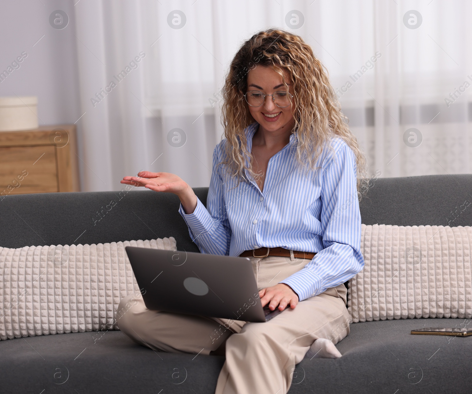 Smiling woman having videochat by laptop on sofa in home office Photo of Smiling woman having videochat by laptop on sofa in home office